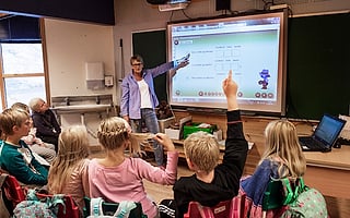 Lærer peker på en interaktiv tavle mens elevene sitter med ryggen mot kameraet