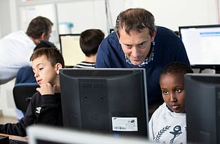 Lærer lener seg over for å hjelpe en elev ved en datamaskin i et klasserom