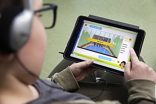 En elev med hodetelefoner følger en « Friends »-lesetime på et nettbrett, med ordet «båt» uthevet i teksten.