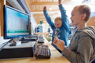 To gutter feirer foran en dataskjerm som viser et mattespill med tall