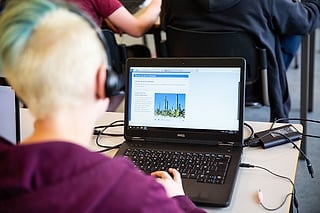 En student med hodetelefoner bruker en Dell-bærbar PC som viser tekst og et bilde av en plante