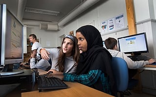 En jente i svart hijab og en klassekamerat ser på en dataskjerm sammen i et klasserom