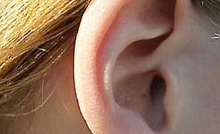 Nærbilde av en persons øre med blondt hår, som illustrerer uttalepraksis